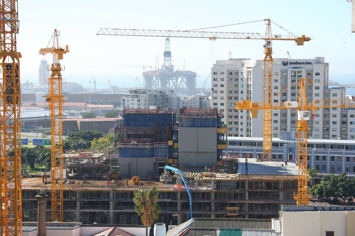 Four tower cranes over a multi-storey reinforced concrete frame under construction in Cape Town, with formwork, props and decks on the lower levels